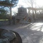 Stone monument with steps in a sunlit park, surrounded by trees and paved ground.