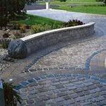 Curved stone bench along a paved garden path with grass and trees nearby