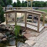 Small wooden footbridge over a stream in a landscaped garden with rocks and stone paving