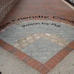 Paved memorial plaque with engraved text set in a brick-bordered walkway
