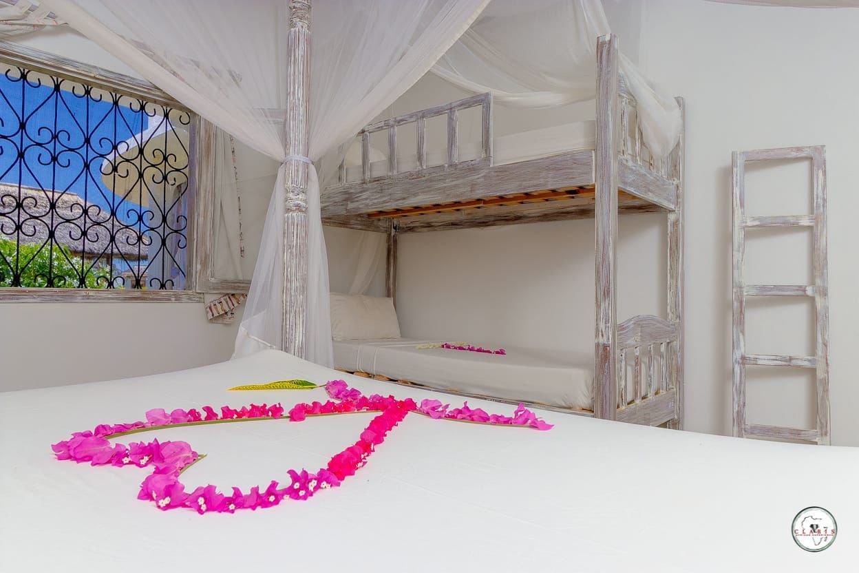White canopy bed with pink heart-shaped flower petals in a bright room by a window