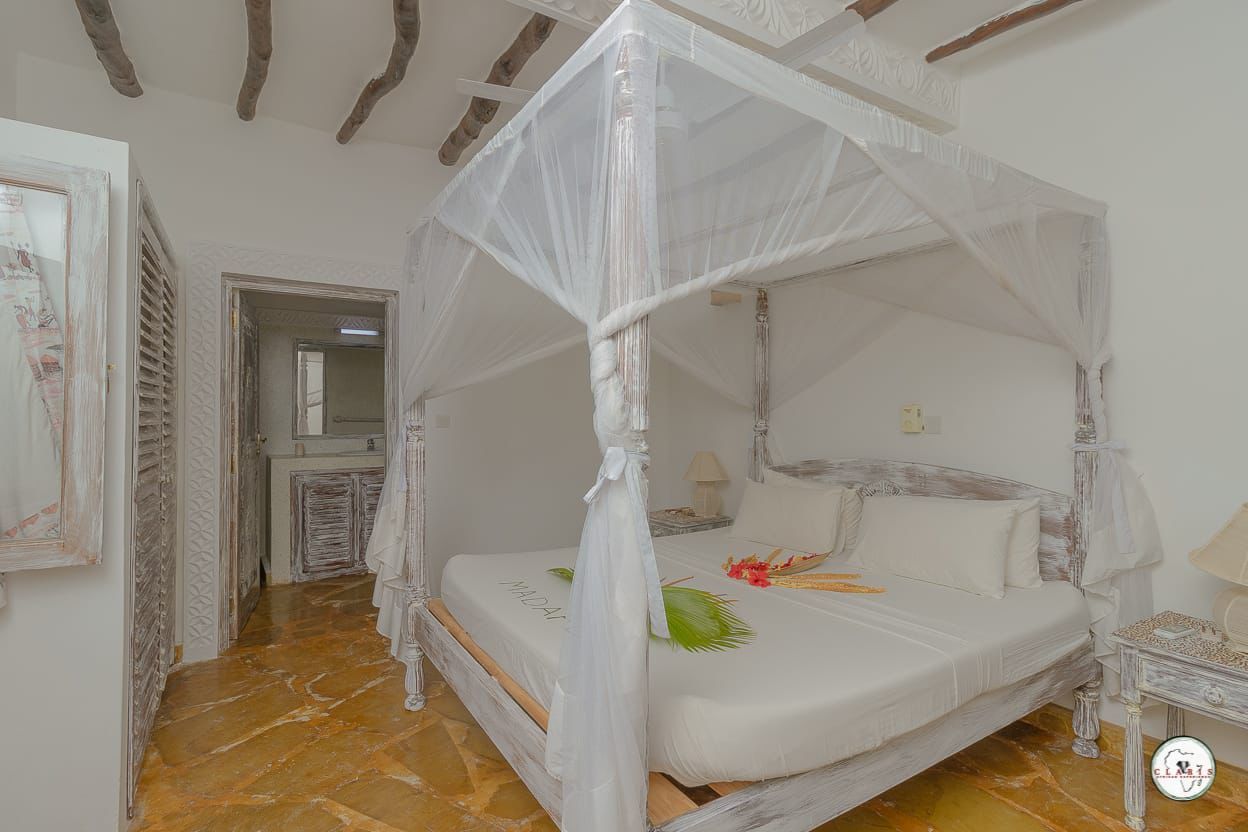 Bright white canopy bed in a rustic bedroom with tiled floor and open doorway