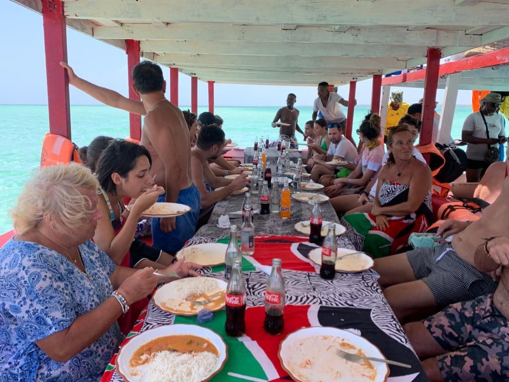 People dining at a long table on a covered beachside deck with ocean views