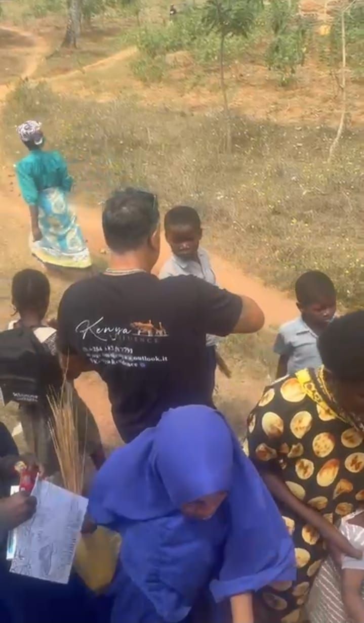 Group walking along a dirt path in a rural area, seen from behind, with a person in teal leading ahead.