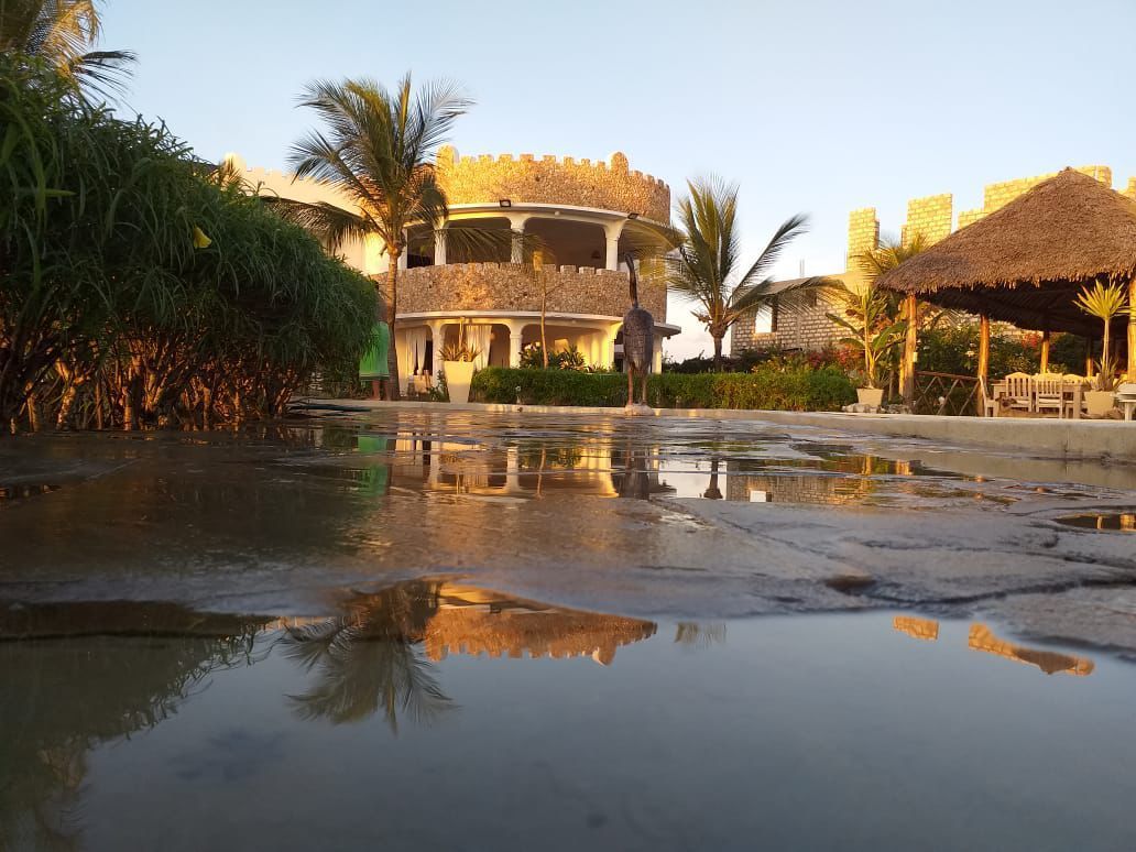 Tropical resort with thatched huts and palm trees reflected in a wet pool at sunset