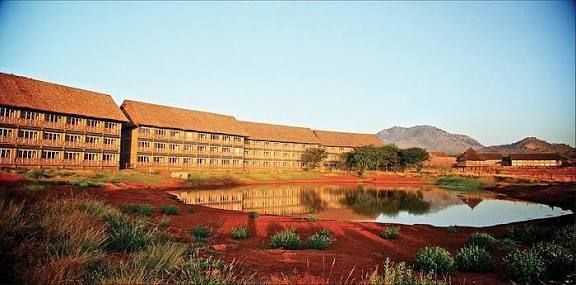 Modern brick buildings beside a red garden and pond under a clear blue sky