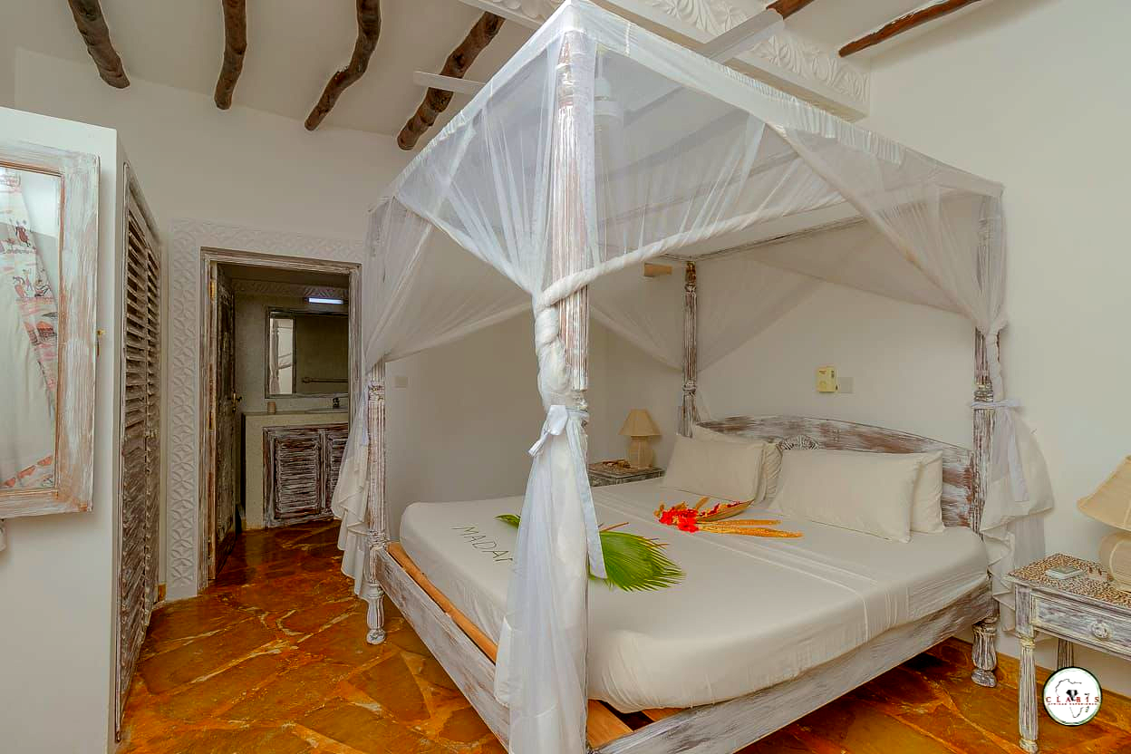 White canopy bed in a bright rustic bedroom with terracotta floor and open doorway