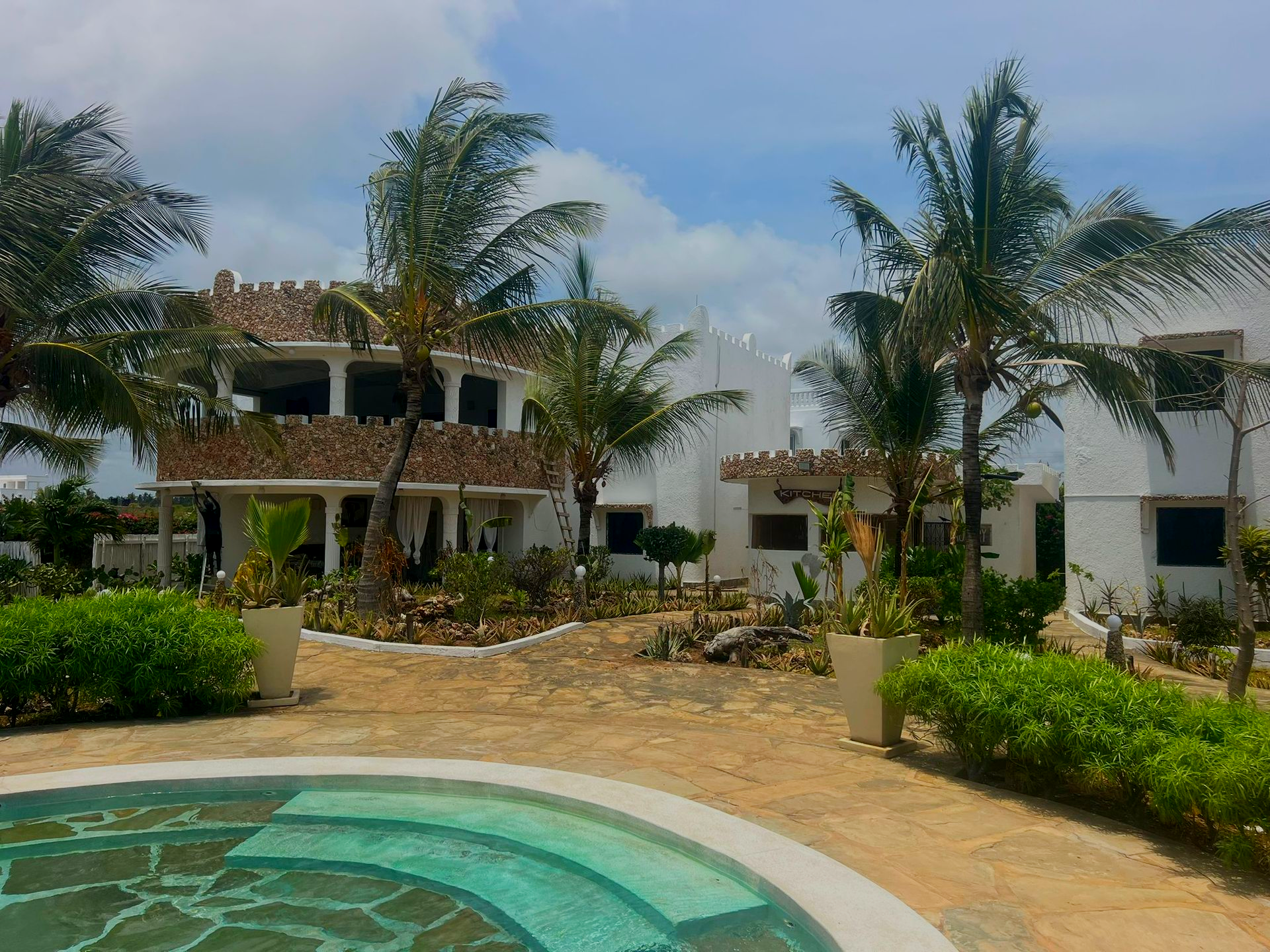 Resort pool with palm trees and white villas under a cloudy sky