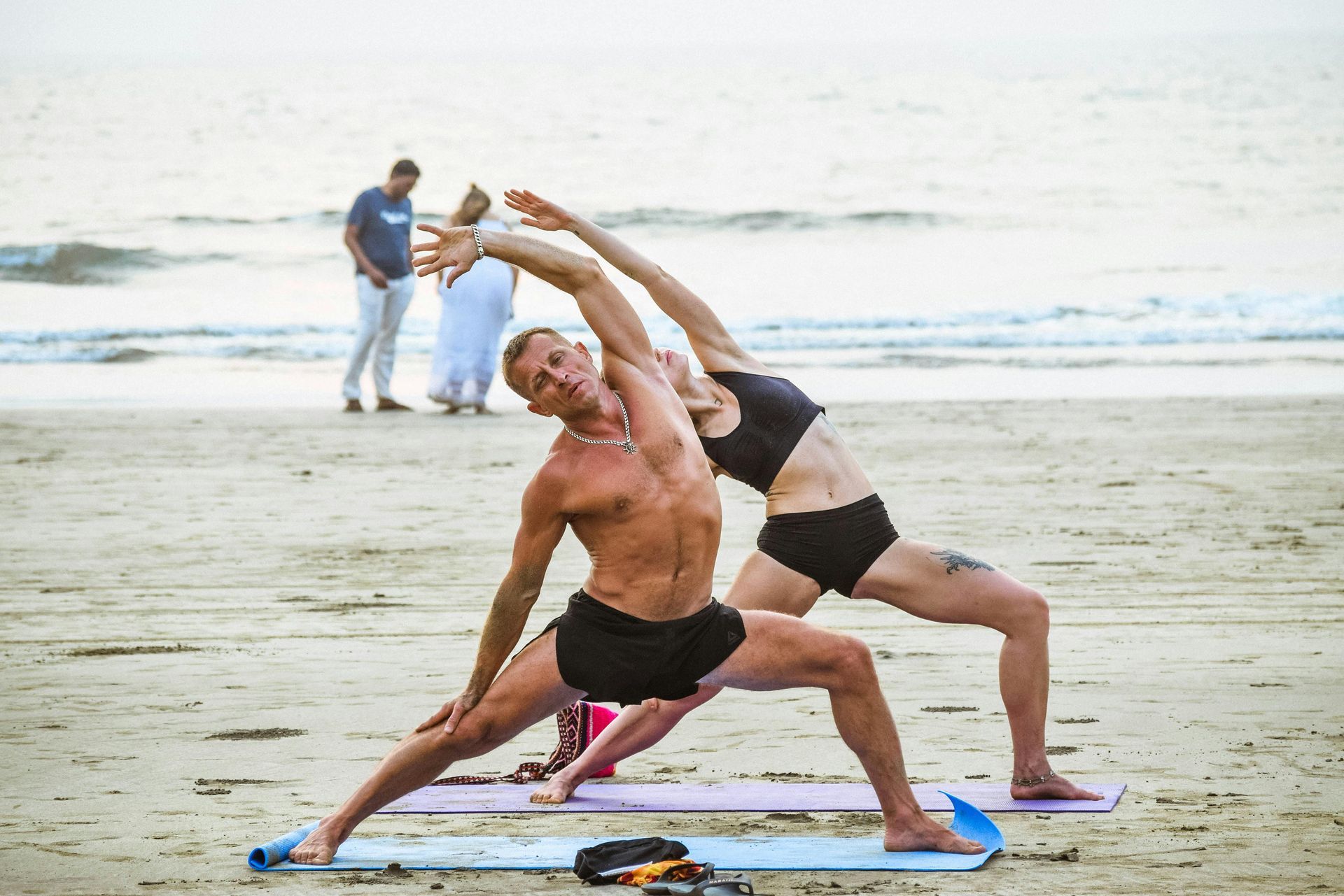 Two people doing partner yoga stretch on mats by the ocean at the beach