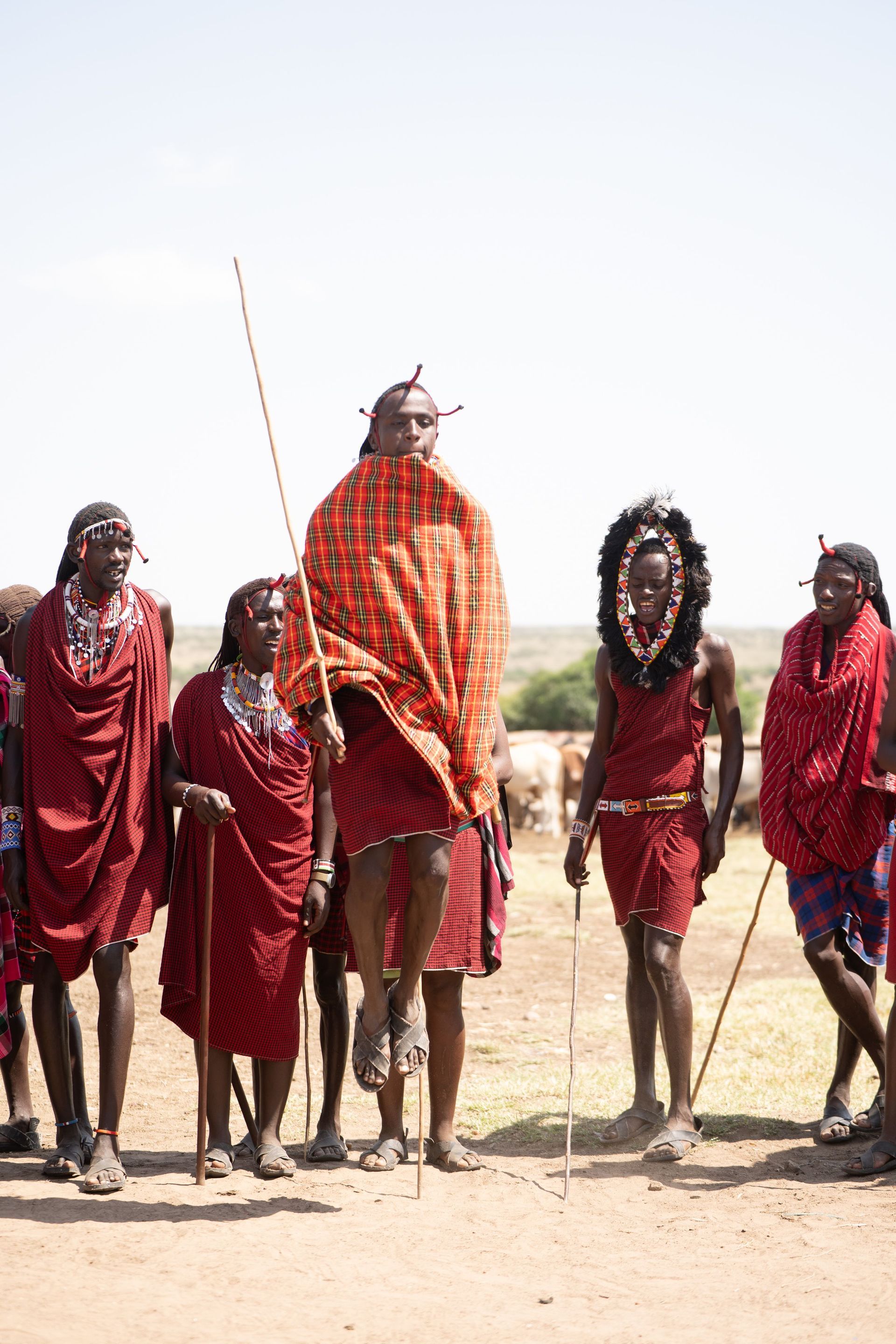A group in bright patterned clothing stands outdoors on sandy ground, with one person holding a staff.