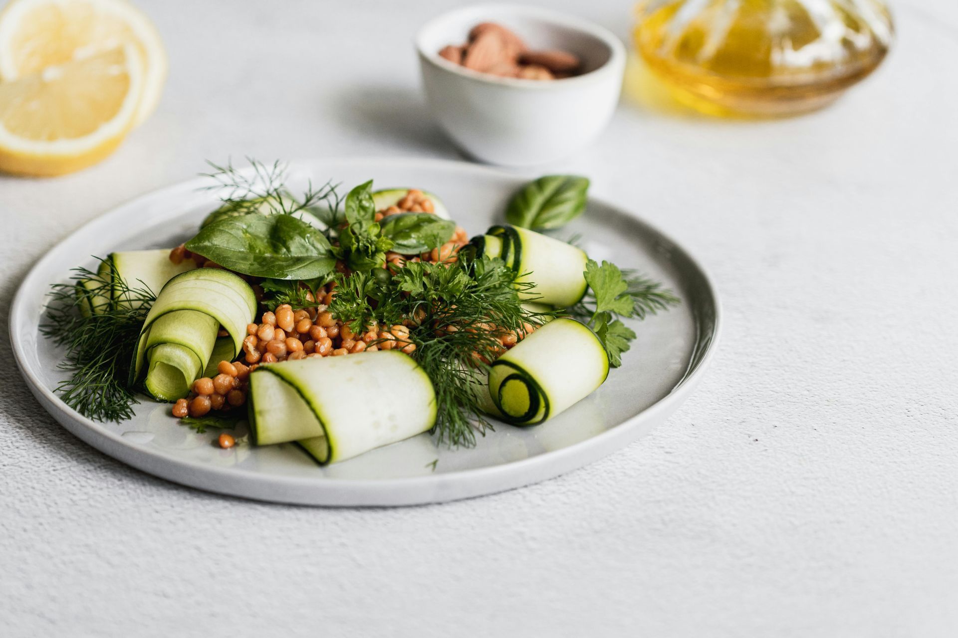 Cucumber roll appetizers topped with dill on a gray plate with a lemon wedge and dipping sauce