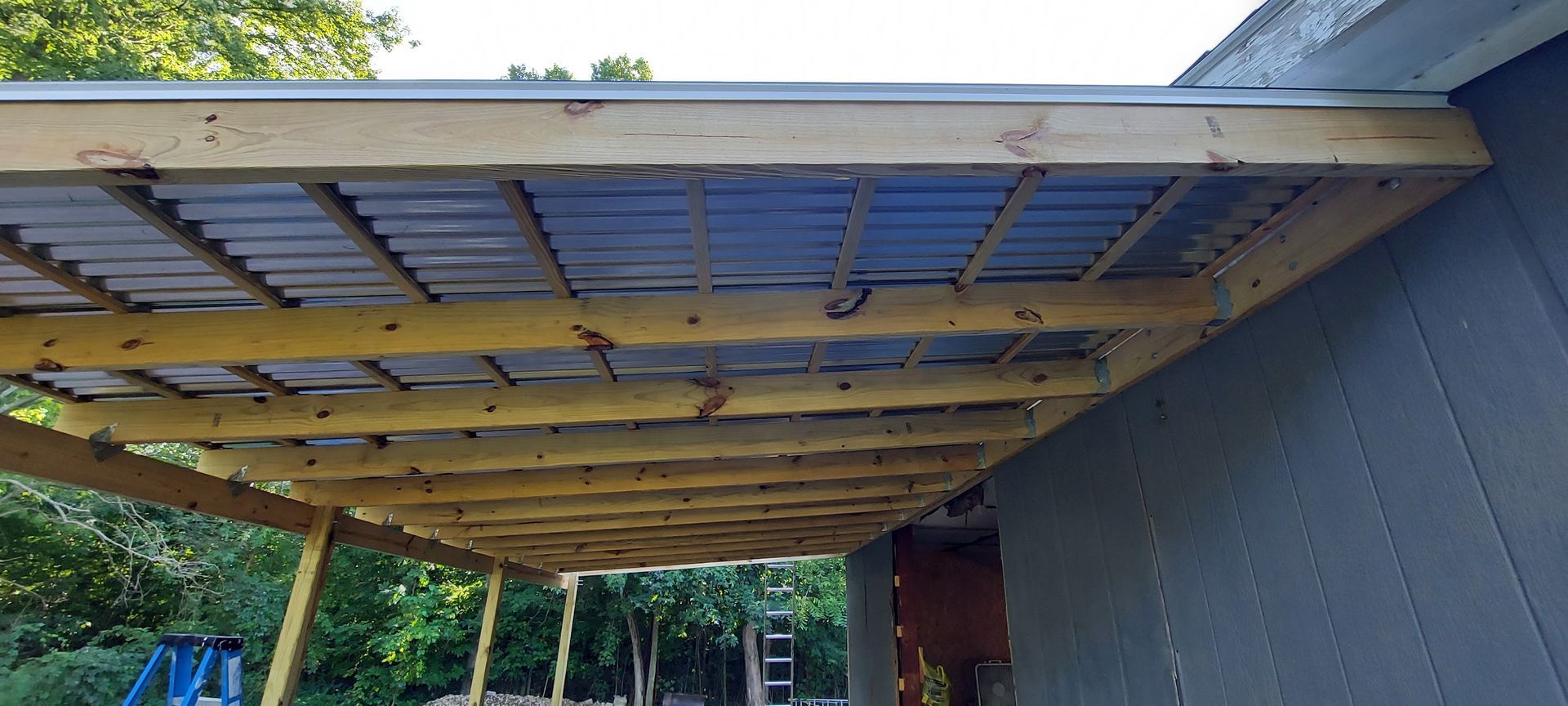 Wooden frame with blue panels forming a roof. Gray building exterior.