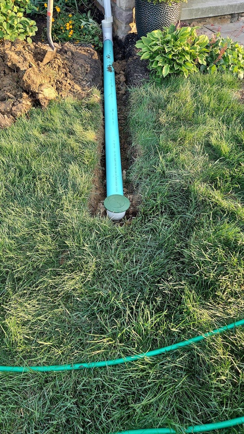 Blue PVC pipe installed in trench in green grass. A green lid and a hose are visible.