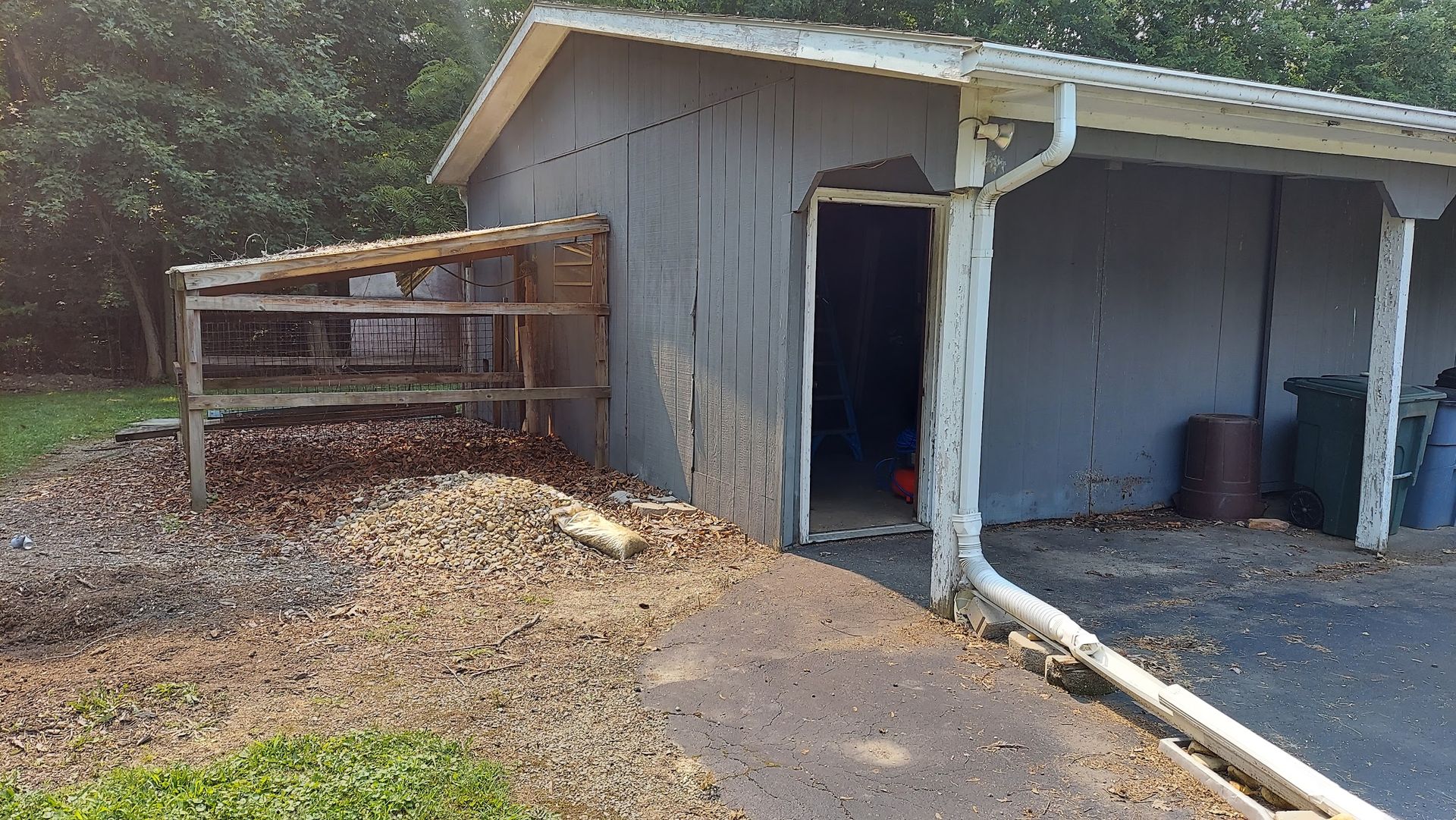 Gray shed with open door and attached lean-to; pathway and pile of debris in front.