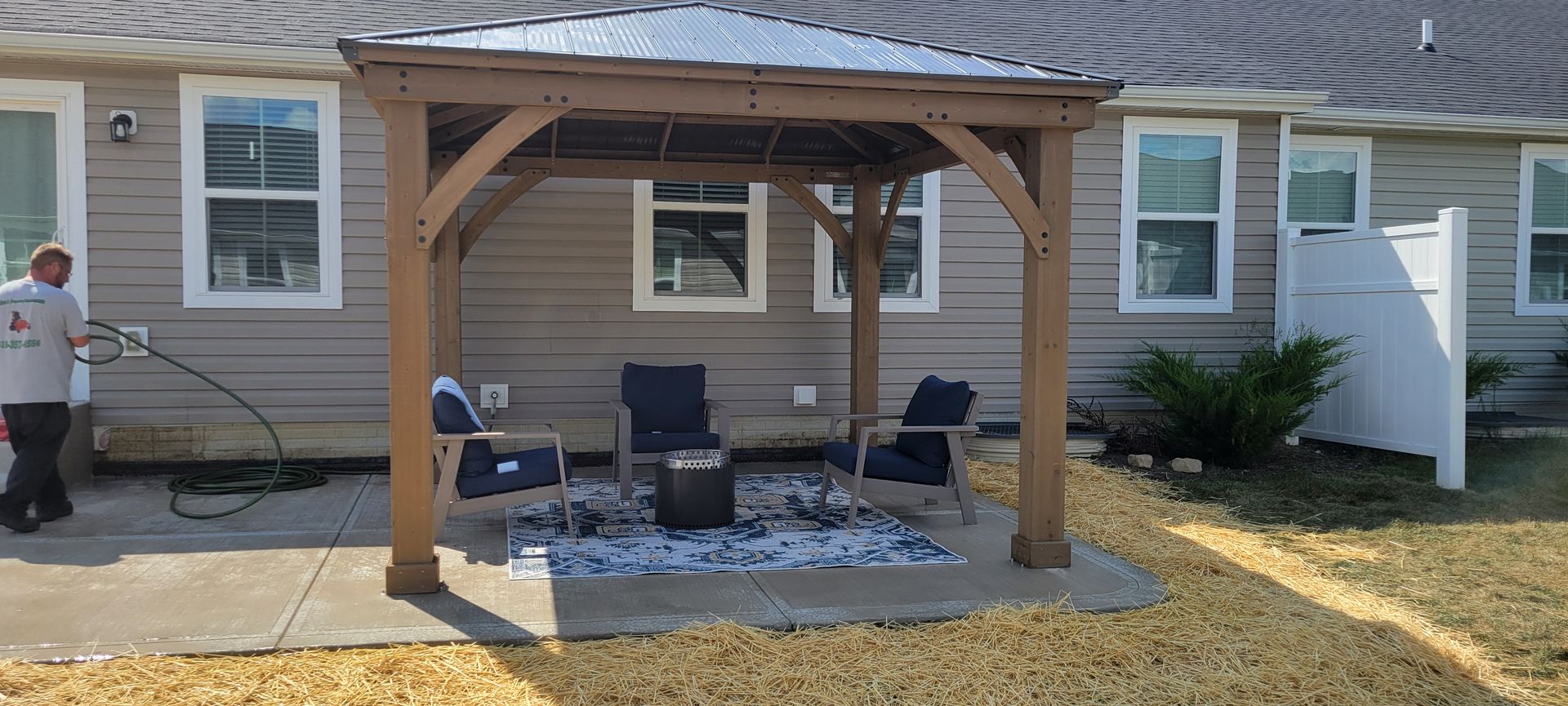 A man is standing in front of a house with a gazebo in the backyard.