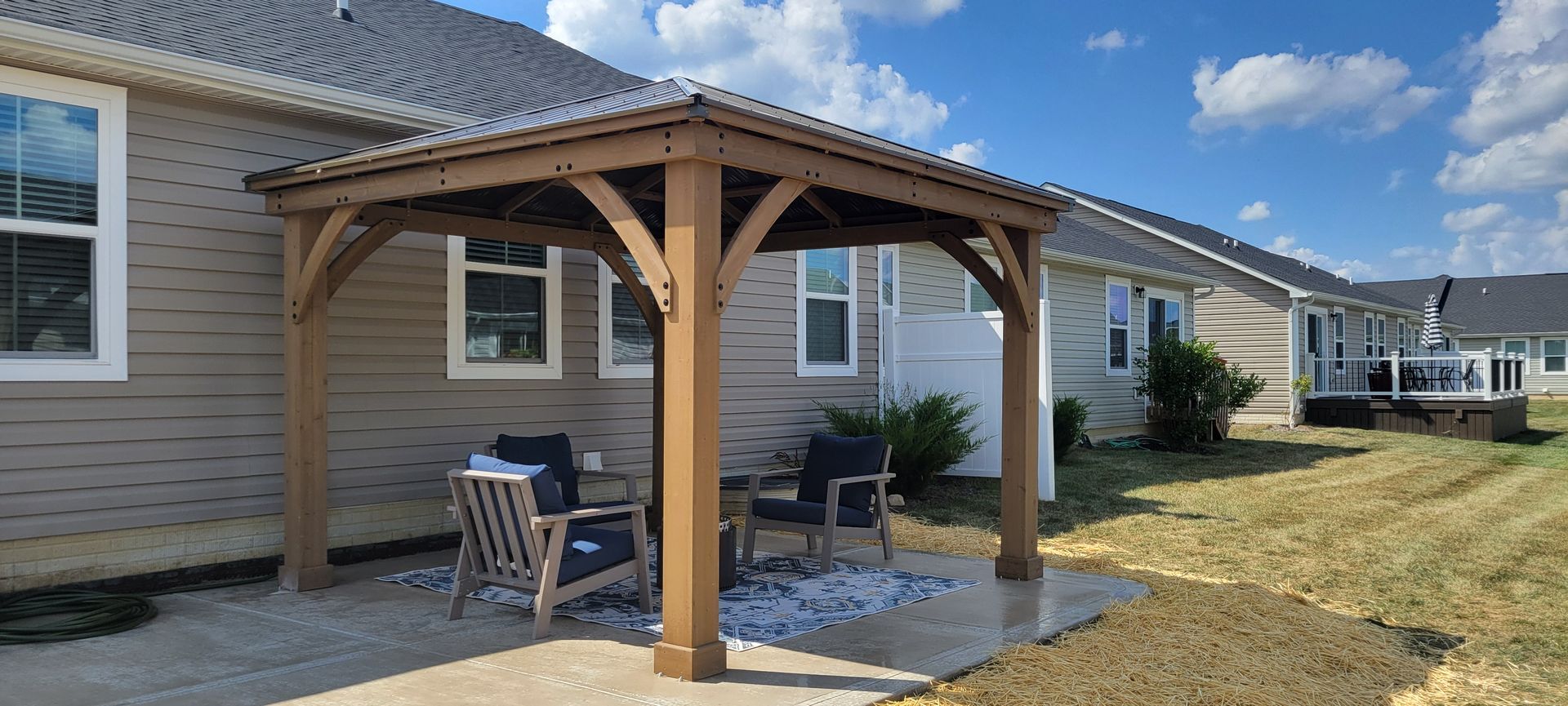There is a wooden gazebo in the backyard of a house.