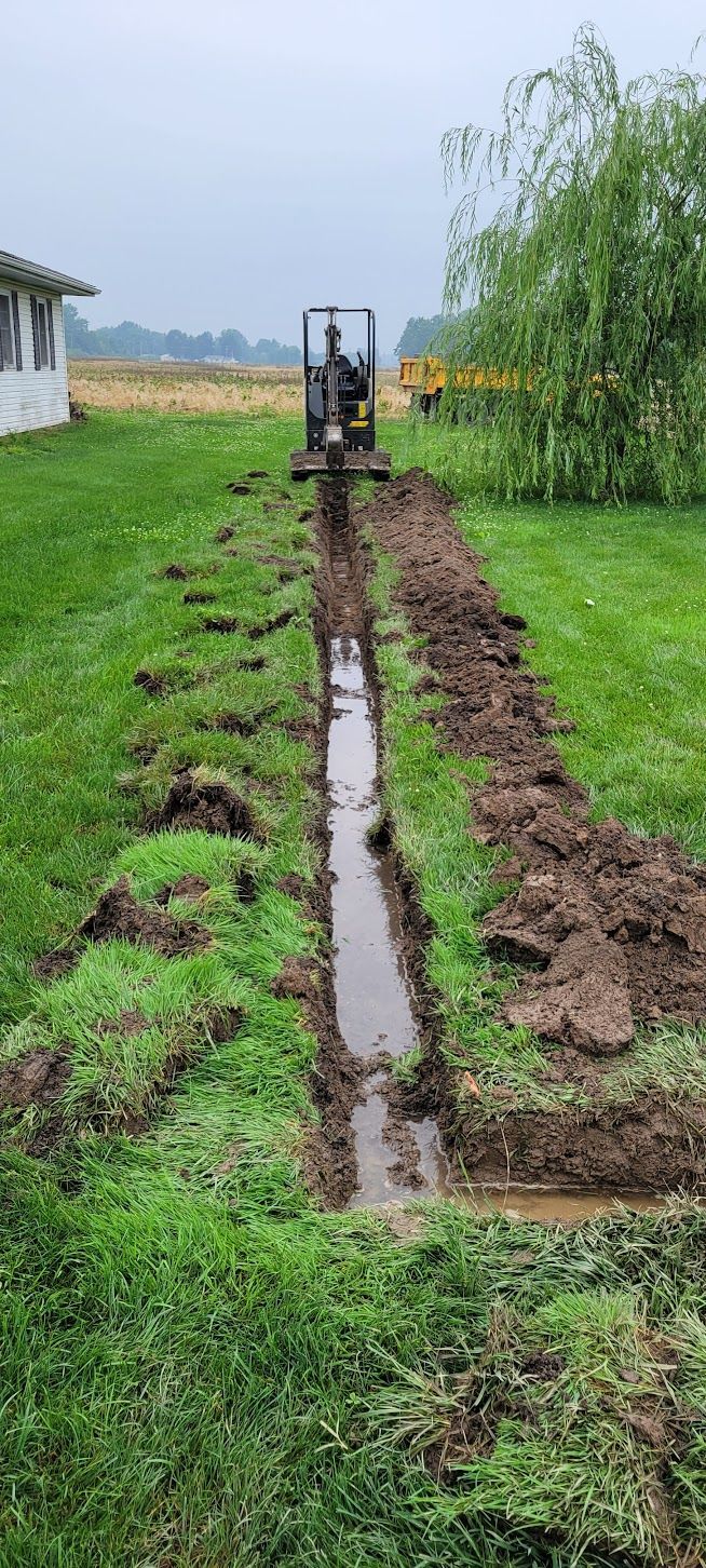 A small excavator digging a trench in a grassy yard, next to a house.