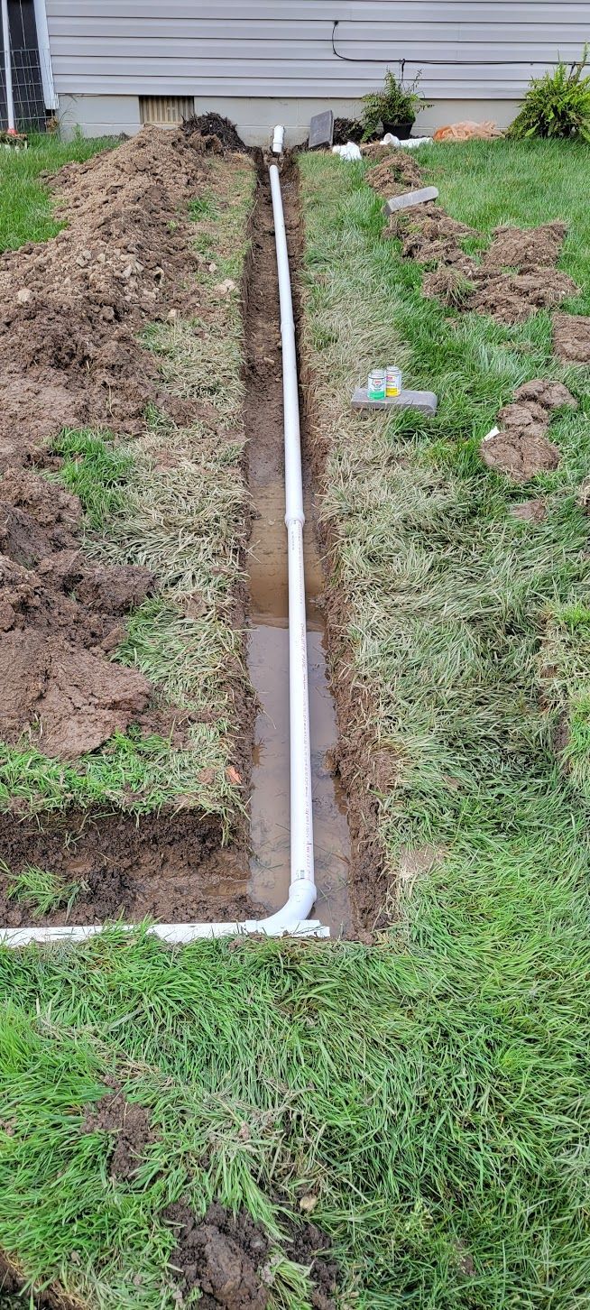 A trench dug in a yard with white PVC pipes laid inside, ready for burying.