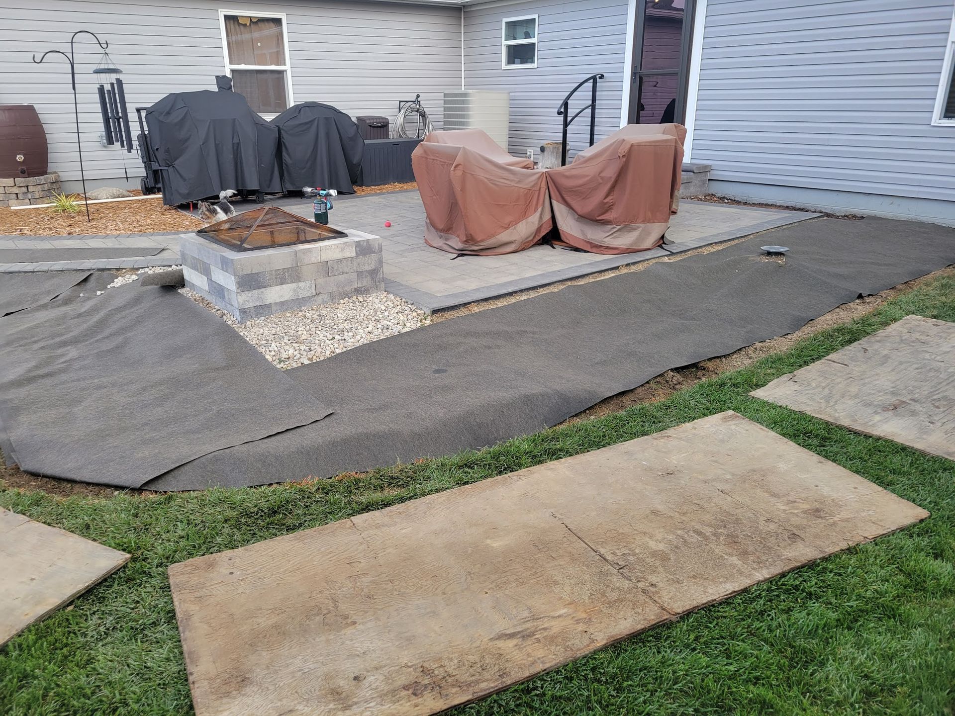 Backyard patio with fire pit, walkway, and covered furniture.