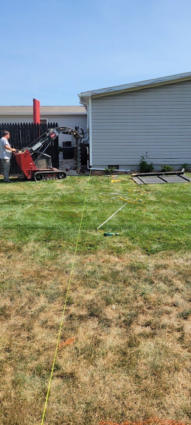 Two people operate a red machine near a building on a grassy lawn under a blue sky.