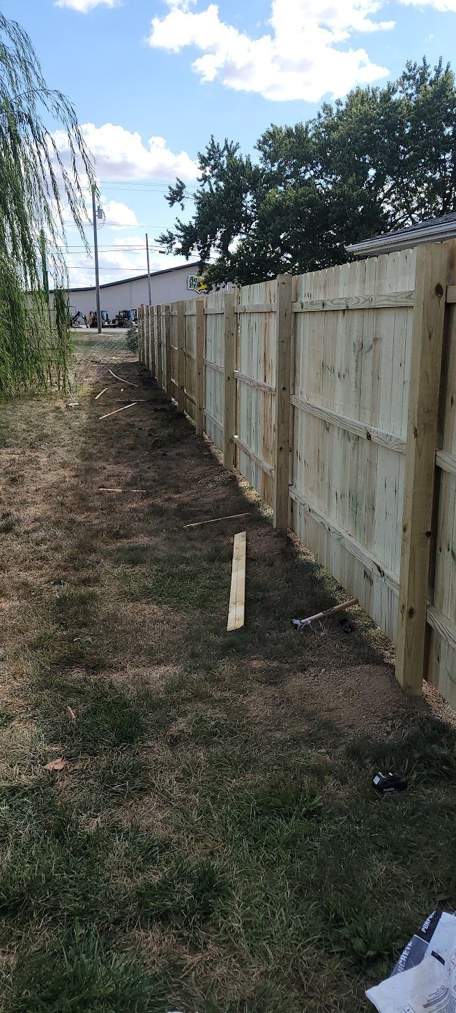 A wooden fence runs along the edge of a yard. Green grass and blue sky.