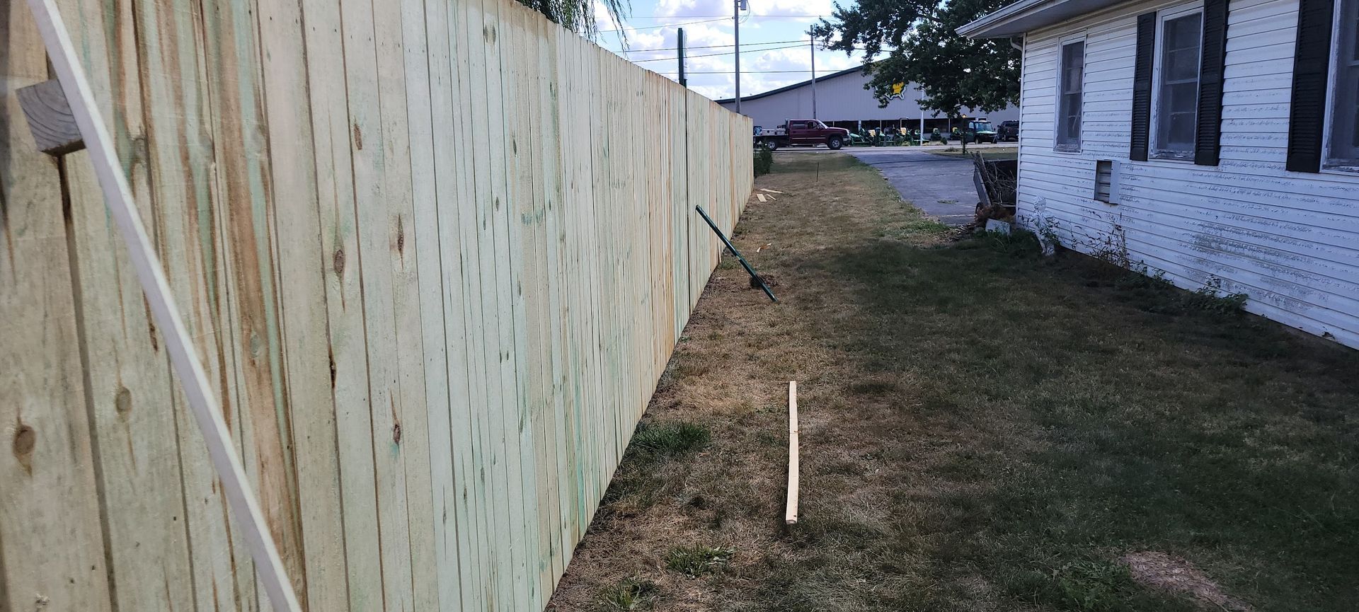 A wooden fence runs along the side of a house with grass in between.