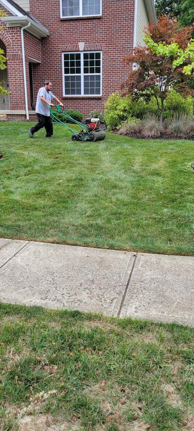 A person mowing a green lawn in front of a brick house.