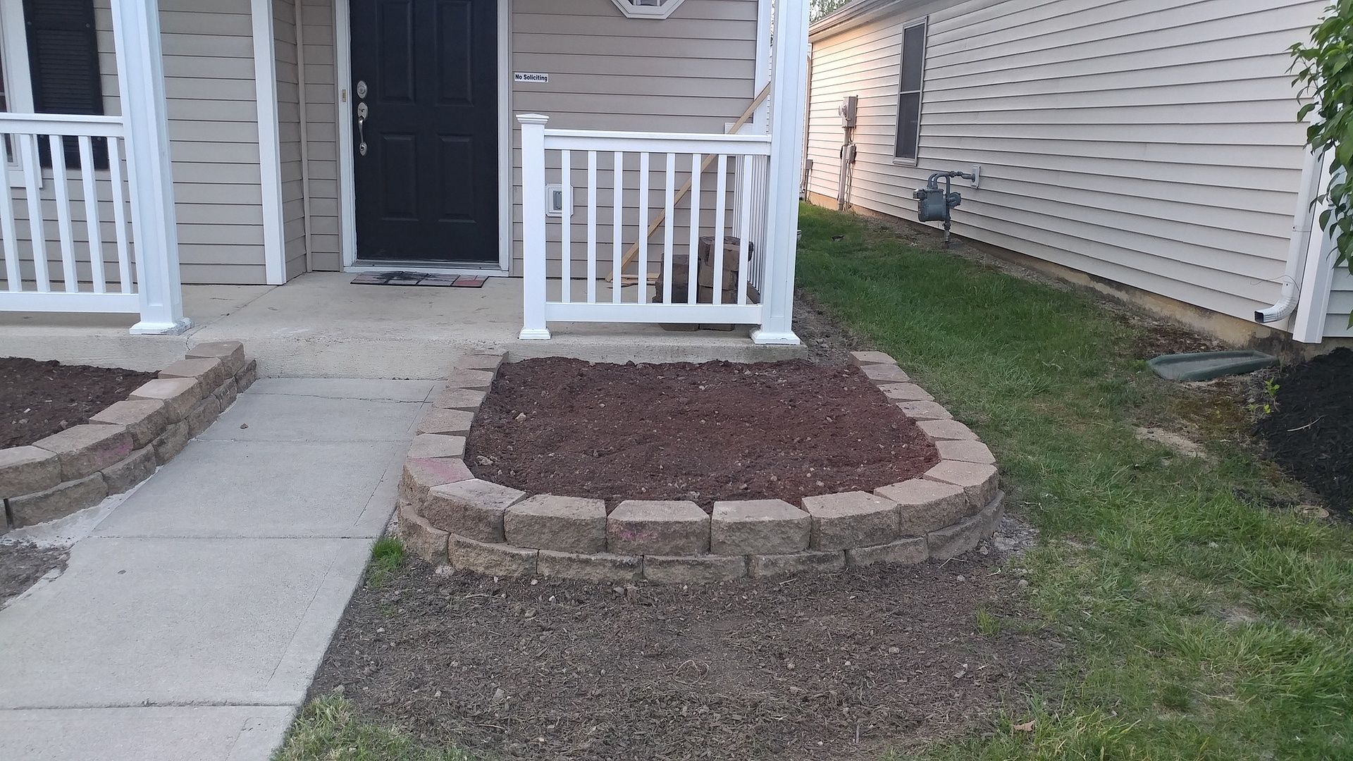 A house with a porch and a brick planter in front of it.