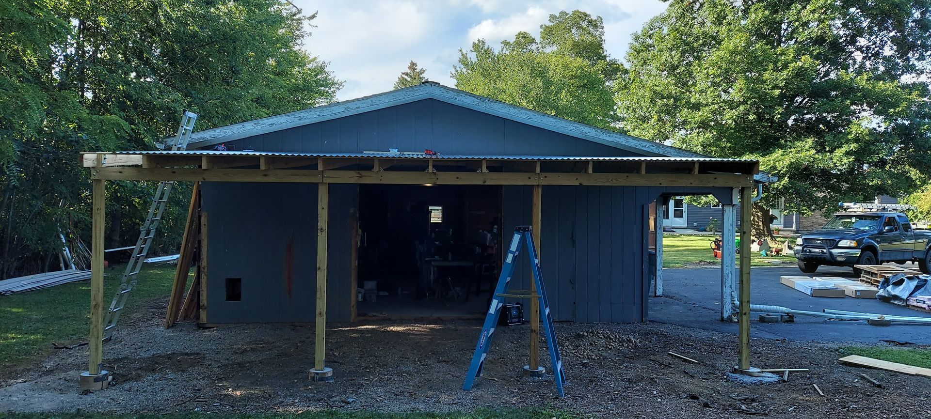 Blue shed under construction with an attached wooden overhang. A ladder is propped up in front.