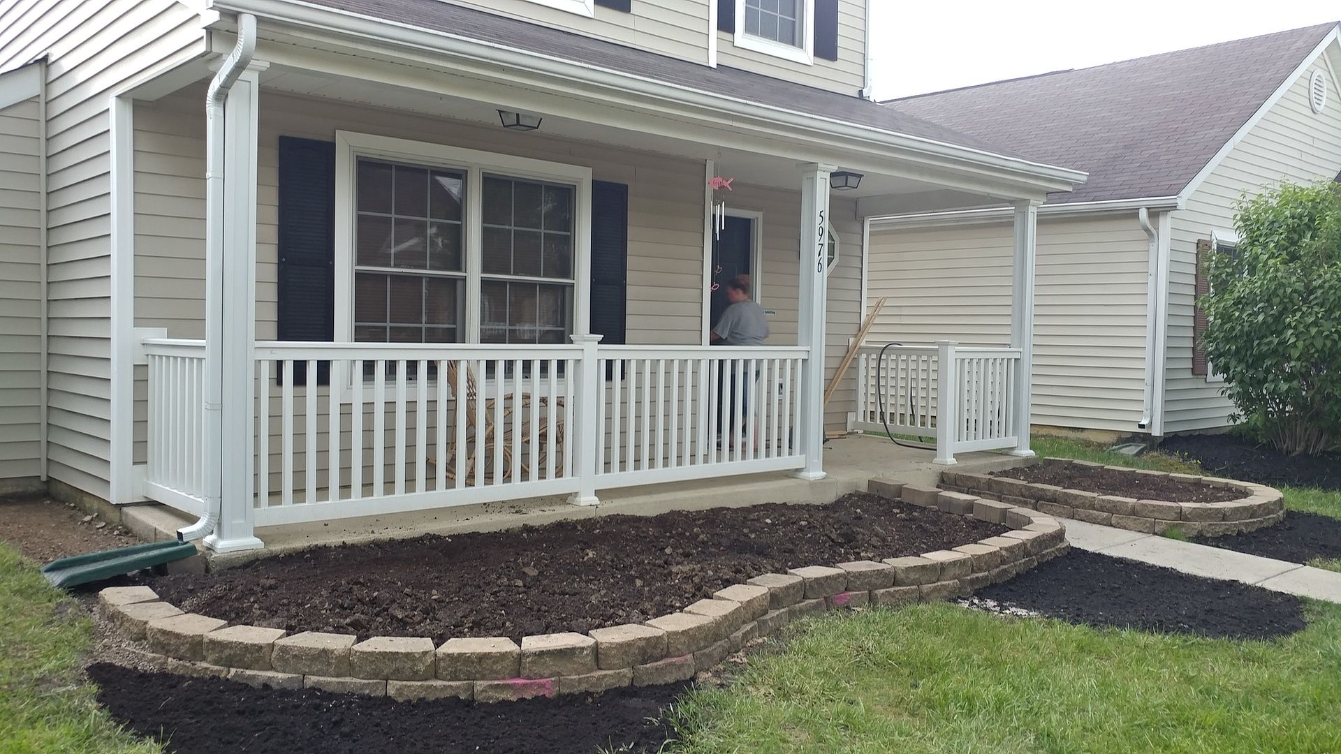A man is standing on a porch of a house with a white railing.