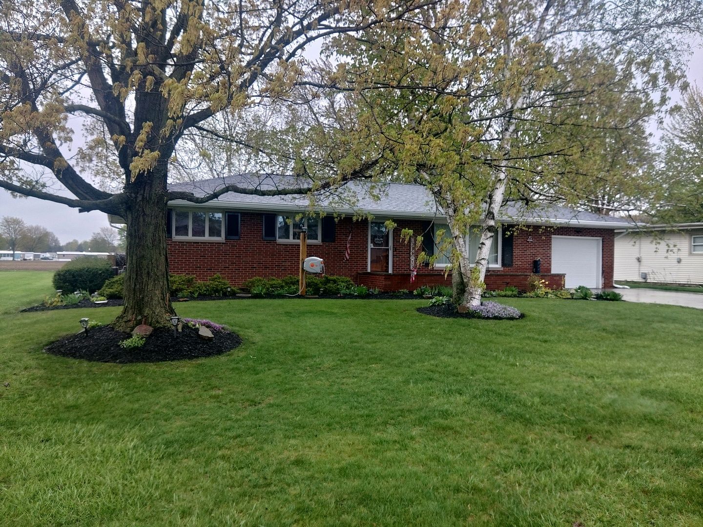 A brick house with a large lush green lawn and a tree in front of it.
