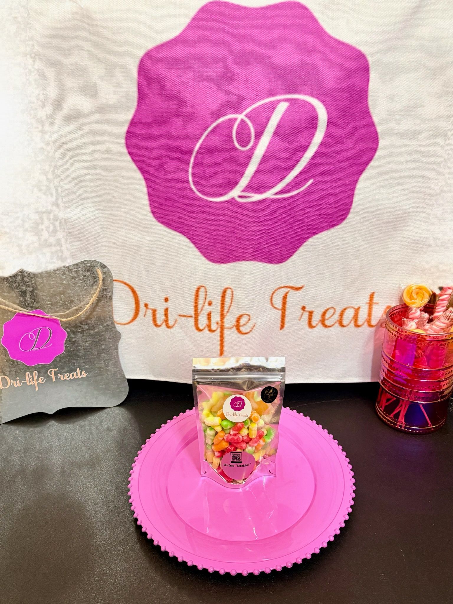 Pink dessert display with monogram logo, branded treat bag, and decorated shot glass on a table.