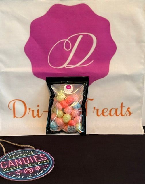 Small clear candy bag with pastel sweets on a white Dri Treats bag with a pink “D” logo.