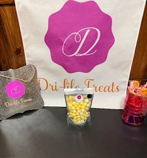 Bags and cups of sweets with a pink “Dri’s Treats” logo display on a table.