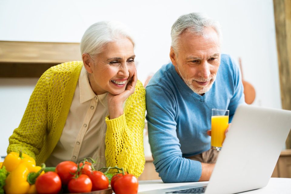 senior couple cooking and looking at computer