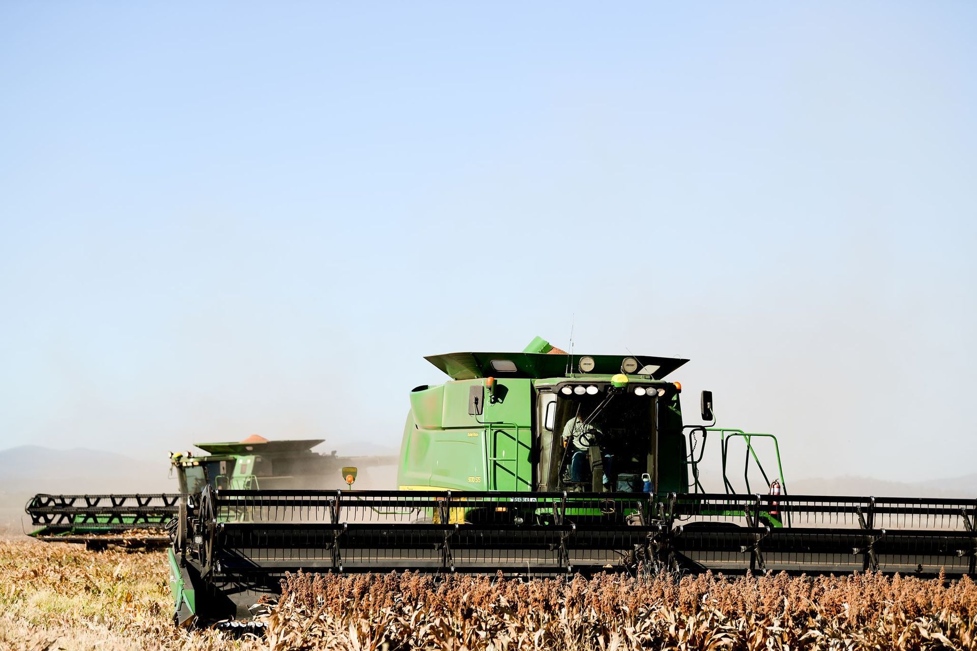 Green combine harvester cutting a cornfield under a clear blue sky