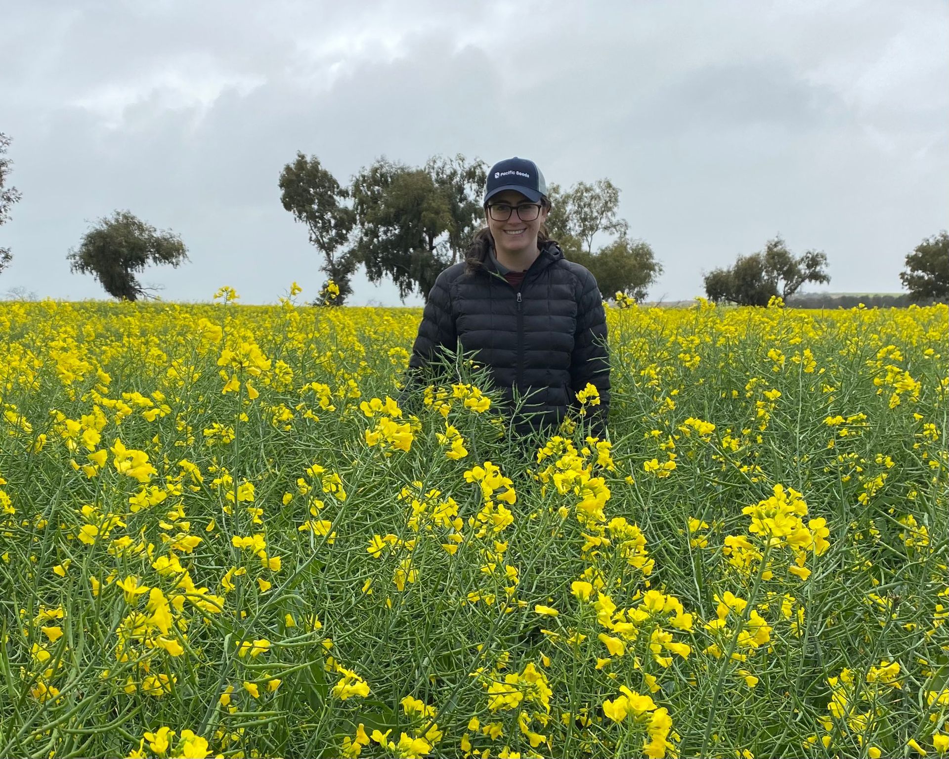 Person standing in a field of yellow flowers under a cloudy sky