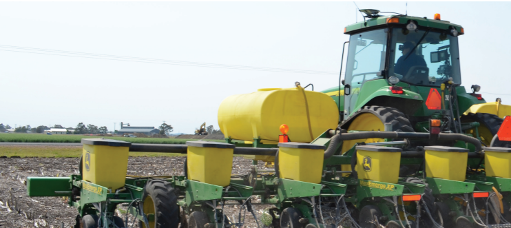 Yellow tractor planting crops in a field with attached seed drills and tanks