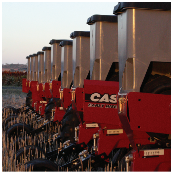 Row of red and silver farm seed planters lined up in a field at sunset