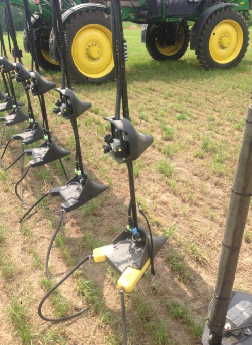 Vertical farm tools with black attachments hanging beside a tractor with yellow wheels in a field