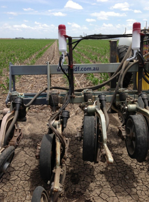 Agricultural boom sprayer with hoses and wheels in a dry field under a blue sky