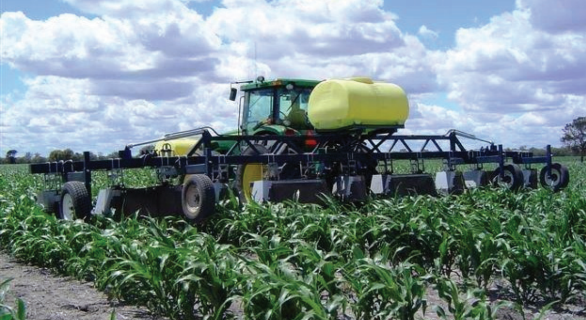 Farm sprayer with yellow tank spraying crops in a green field under a cloudy sky
