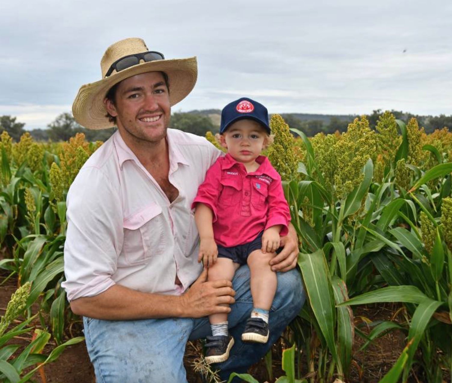 Man in a straw hat holding a child in a cornfield, both facing the camera.