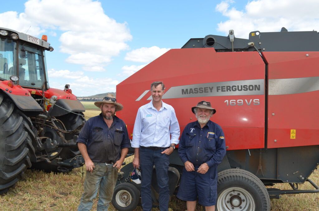 Three people posing beside a red Massey Ferguson tractor and baler in a farm field.