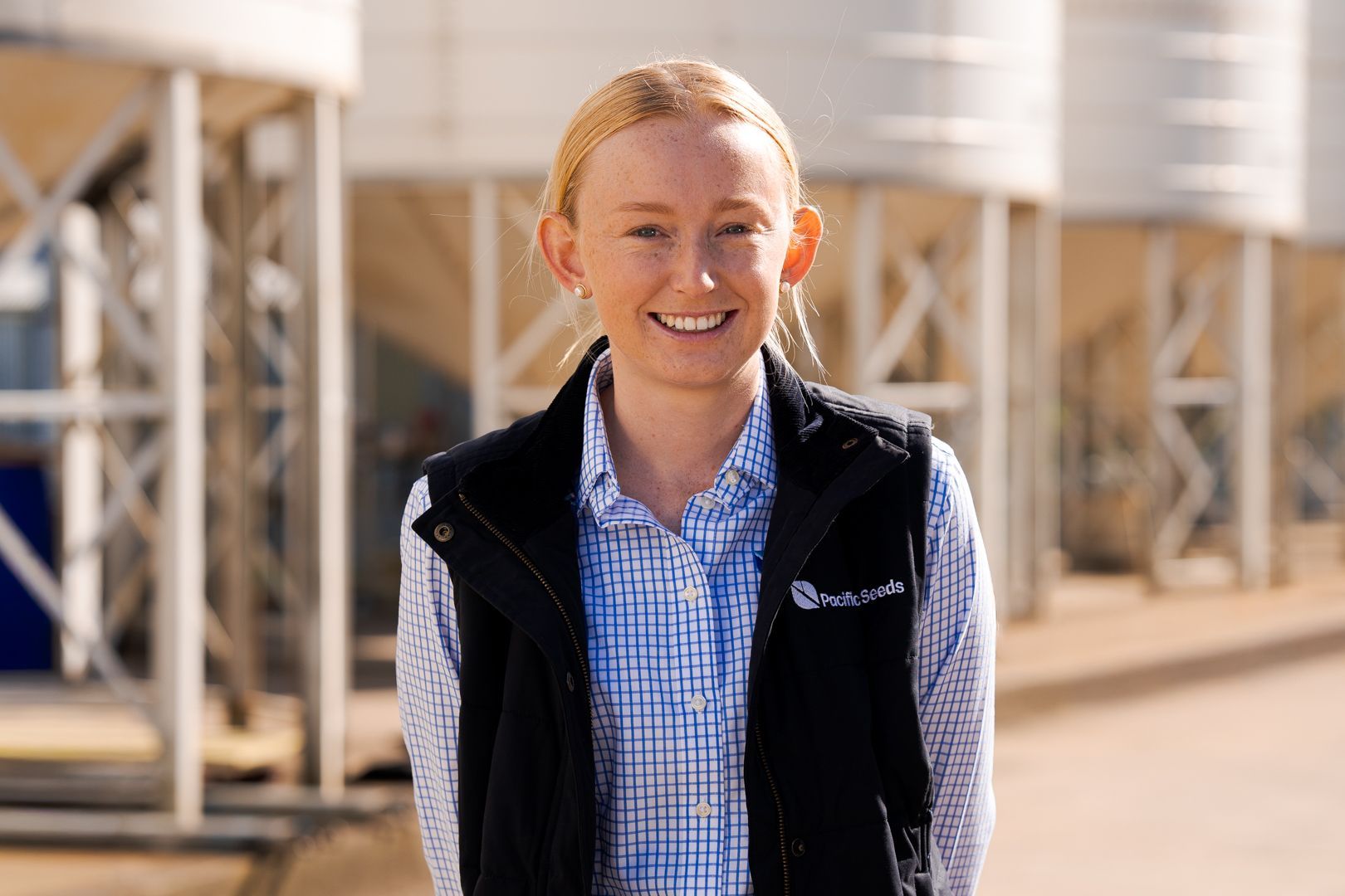 Person smiling in a black vest and blue checkered shirt at an industrial site