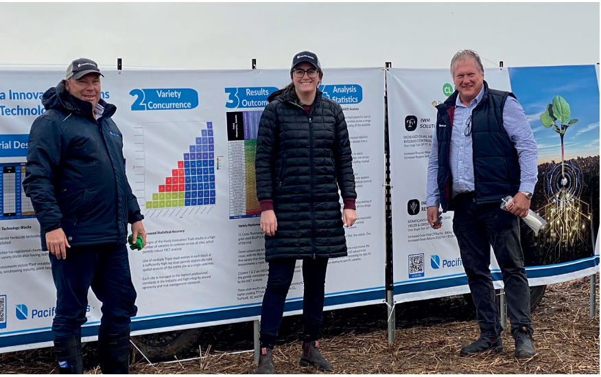 Three people stand in winter coats beside informational banners outdoors.