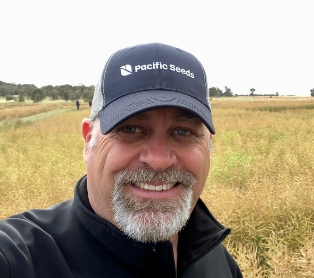 Smiling man in a navy cap and black jacket standing in a grassy field