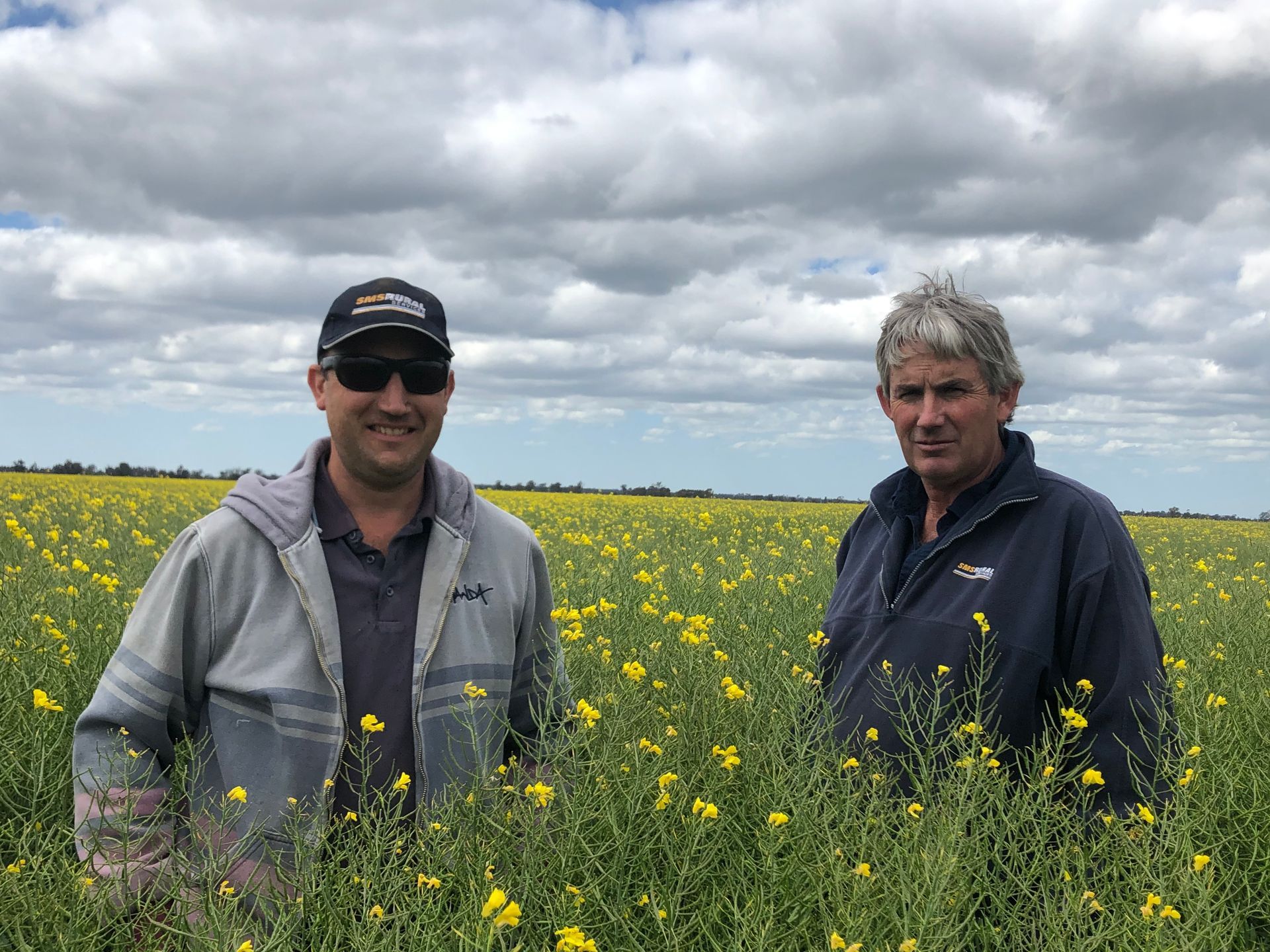 Two people standing in a yellow wildflower field under a cloudy sky