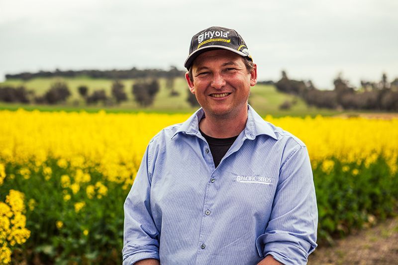 Smiling man in a blue shirt and cap standing in a yellow flower field