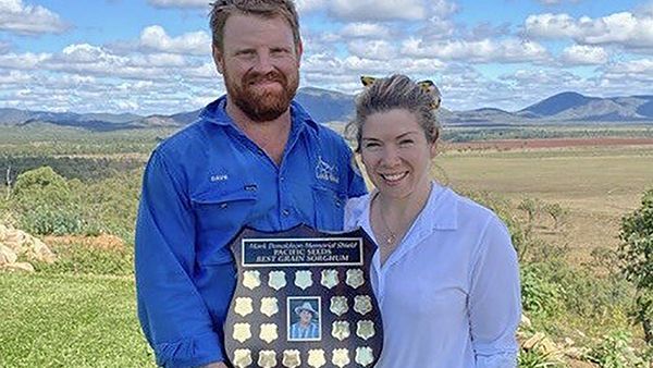 Two people holding a plaque outdoors with mountains in the background